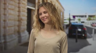 Kadın saçı, gülümseyen yüz olarak akar sokak sahnesini aydınlatır. Sarışın genç deneğin şehir ortamında doğal tonlarda poz verdiği sahne..
