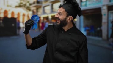 İspanyol asıllı bir adam, aşçılık başarısını ve başarısını simgeleyen, hareketli bir caddede ödül kurdelesini gururla sergiliyor..
