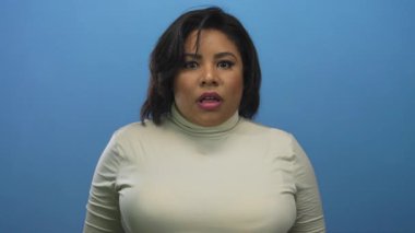 Genç, iri yarı, İspanyol bir kadın mavi izole bir arka planda şaşkınlık yaşıyor..