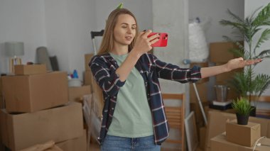 Yeni bir eve selfie çeken bir kadın. Odasında paketlenmemiş kutular var. Etrafı bitkilerle çevrili.