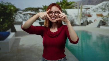 Oteldeki havuzun yanında gülümseyen bir kadın elleriyle yüzünü çerçeveliyor ve rahat bir atmosfer yaratıyor..