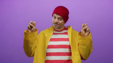 Sarı yağmurluk giyen, çizgili gömlekli genç adam canlı mor bir arka plana karşı jestler yapıyor..
