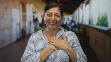 Orta yaşlı, çizgili tişörtlü, göğsünde güneş ışığıyla gülümseyen İspanyol kadın..