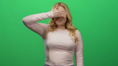 Parlak yeşil arka planda elleri olan, pembe uzun kollu bluz giyen ve gülümseyen genç ve neşeli bir atmosfer yaratan bir kadın..