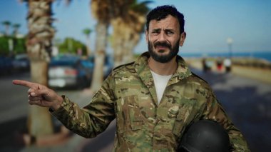 Askeri üniformalı İspanyol bir adam, güneşli bir caddede arka planda palmiye ağaçları olan ve yönünü ve amacını bildiren açık havayı işaret ediyor..