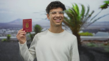 Gülümseyen ve elinde kırmızı Danimarka pasaportu olan genç adam gün ışığında bulanık tepelerle caddede seyahat heyecanı.