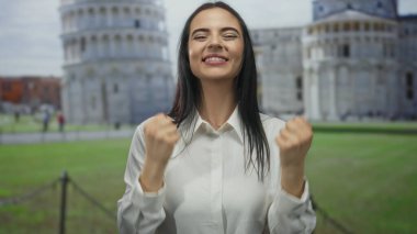 İkonik pisa kulesinin önünde yumruklarını sıkarak mutlu bir şekilde tezahürat eden kadın, canlı açık hava atmosferini ve İtalyan kültürel özünü yakalıyor..