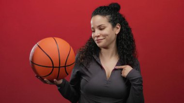 Elinde basketbol topu tutan kadın kırmızı arka planda kendine güvenini ve kararlılığını gösteriyor..