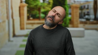 Sakallı, beyaz bir adam şehir merkezinde bir sokakta boyun ağrısı çekiyor, dışarıda rahatsızlığını dile getiriyor..