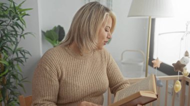 Sarışın kadın yatak odasındaki sıcak lambanın altında hareketli beşiği olan masal kitabı okuyor. Huzur..