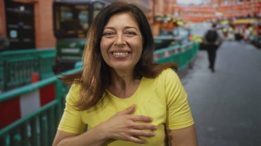 Sarı tişörtlü kadın ağzı açık gülümsüyor ve inşaat bariyerinin yakınındaki caddeyi işaret ediyor. Mutluluk..