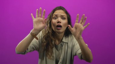 Duygularını canlı pembe arka plana karşı kaldıran kadın, tecrit ortamında sürpriz ve aciliyeti ifade eder.