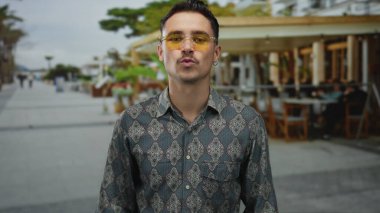 Genç İspanyol adam kalp hareketi yapıyor ve teras caddesindeki bir açık kahve restoranında öpücük yolluyor..