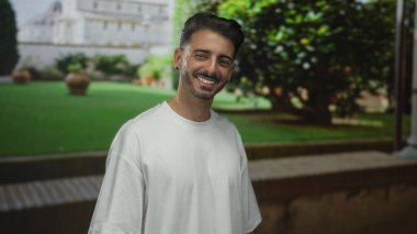 Yüzünde yeşil çimenler ve kilden tencereler olan tarihi bir binanın yanında dişlerini gösteren adam gülümsüyor. Mutluluk..