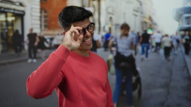Gözlüklü genç adam hareketli bir şehir caddesinde poz veriyor bulanık yayalar, şehir enerjisi ve canlı şehir hayatı sergiliyor..