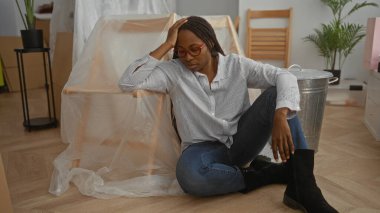 Yeni ev oturma odasında dinlenen bir kadın paketlenmemiş kutularla çevrili, yere yakın otururken bitkin hissediyordu..