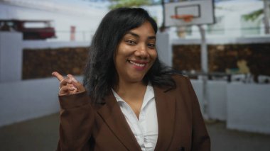 Kadın açık hava basketbol sahasında beyaz gömlek giyerek zafer işareti gösterirken geniş bir gülümseme sergiliyor; barış umudu birliği.