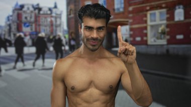 Genç, İspanyol gömleksiz bir adam, arka planda gezginler ve kalabalık şehir caddesinde ileriyi işaret ediyor..