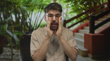 Yeşilliğe tepeden bakan bir merdivenin yanındaki modern bir binanın lobisinde elleri ağıza dolamış ve temiz bir sesle bağırıyor; acil uyarı uyarısı.