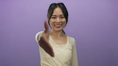 Gülümseyen bir kadın, mor bir arkaplan karşısında arkadaşça bir ifadeyle elini uzatarak izole edilmiş bir stüdyoda evrensel bir hoş geldin jesti sergiliyor..