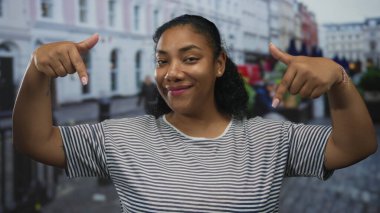 Kadın gülümsüyor ve her iki işaret parmağı da bulanık şehir binaları arasında caddede aşağı doğru; coşku.