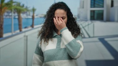 Plaj gezisindeki kadın sıcak süveteri ve okyanus altyapısı ile rahatsızlığını dile getiriyor. Güneşli bir günde palmiyelerin ve modern mimarinin huzurlu manzarasını yakalıyor..