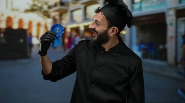 İspanyol asıllı bir adam, aşçılık başarısını ve başarısını simgeleyen, hareketli bir caddede ödül kurdelesini gururla sergiliyor..