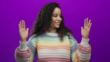 Kıvırcık saçlı, elleri mor arkaplan üzerinde hareketli pastel renkli gökkuşağı süveter giyen kadın.