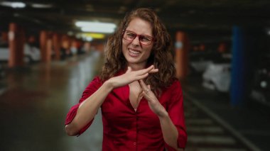 Kapalı otoparkta mola veren genç, kıvırcık saçlı ve gözlüklü bir kadın..