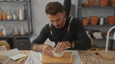 İnsan, çömlek aletleriyle çevrili bir stüdyoda, ahşap bir masada elleri ile çiğ kil kaseyi şekillendirir; yaratıcı konsantrasyon.