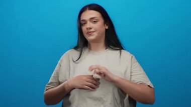 Genç, iri yarı bir kadın, mavi bir duvara yaslanmış, elleri birbirine kenetlenmiş, düşünceli bir ifade sergiliyor..