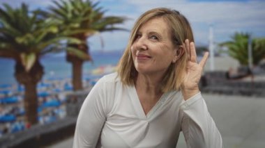 Kadın el ele tutuşup öne eğiliyor ve kumlu sahilde palmiye ağaçlarının arkasını dinliyor; merak.