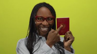 Kırmızı gözlüklü, sırıtan kadın sarı arka planda parlak pasaport taşıyor..