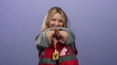 Kırmızı yelekli, mor arka planlı, gülümseyen gönüllü bir kadın yardımsever bir ortamda coşku ve pozitiflik gösteriyor..