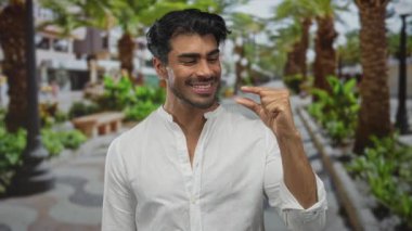 Adam, palmiye ağaçları ve bankları olan yeşil bir parkta başparmak ve işaret parmağı çimdikler; hassasiyet ölçümü.