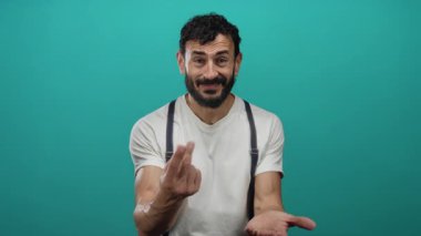 Sakallı, beyaz gömlek ve pantolon askısı takmış, el hareketleri ve yüz ifadeleriyle duygularını ifade eden İspanyol asıllı bir adam..