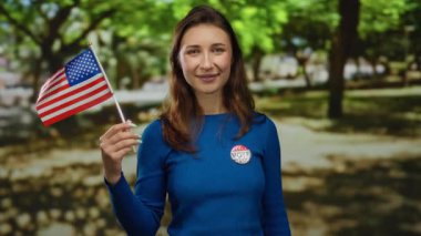 Parkta elinde Amerikan bayrağı ile gülümseyen bir kadın seçim kampanyası sırasında vatanseverlik rozeti takıyor..