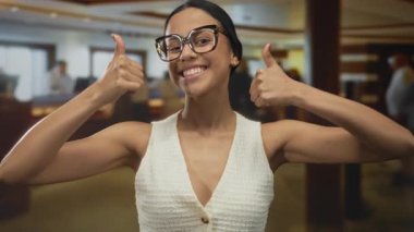 Mutlu kadın otelin lobisinde olumlu bir tavır sergiliyor. Büyük bardaklar ve gülümseyen yüz ifadesi kapalı mekan atmosferini ve konukseverliği arttırıyor.