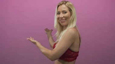 Kırmızı dantelli sutyen giyen kadın çıplak omzunu gösteriyor ve pembe stüdyoda avuç içleriyle sunuyor..