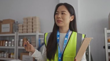 Yansıtıcı yelek giyen bir kadın, bir hayır kurumunun gönüllü merkezinde, malzeme ve kutularla çevrili, kapalı bir toplulukta vicdani bir ruhu somutlaştıran bir pano tutuyor..