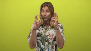 Çiçekli gömlek giyen uzun saçlı sarışın adam, parlak yeşil stüdyoda çıplak elleriyle çapraz parmaklar tutuyordu..