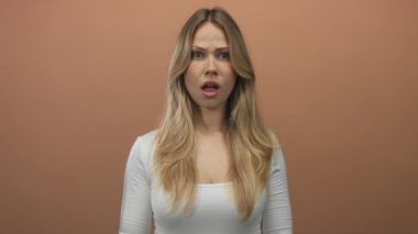 Sarışın, beyaz bir kadın şeftali arkaplanlı fotoğraf stüdyosunda işaret parmağıyla göğsünü işaret ediyor..