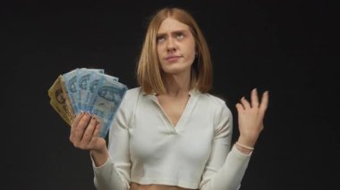 Genç bir kadın, mali bir ikilemi tasvir eden, siyah bir geçmişe karşı karışık bir ifadeyle Macar forint banknotları tutuyor..