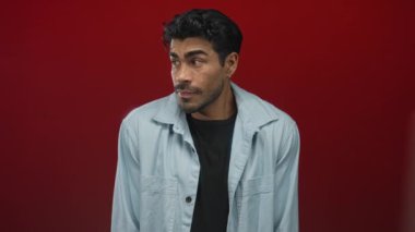 Açık renk kot gömlek giyen İspanyol genç adam stüdyoda içten bir sırıtışla gülümsüyor..