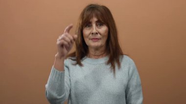 Üst düzey İspanyol kadın kafaya dokunan süveter giyiyor. Kahverengi bir duvarın önünde düşünceli bir yüz ifadesi var. İç gözlem ve tefekkür olduğunu gösteriyor..