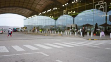 Şehirdeki ulaşımı ve bokeh efektlerini gösteren odaklanmış arka planla büyük havaalanı terminalinin dışında yürüyen bulanık insanlar.