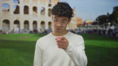 Genç İspanyol adam parlak güneş ışığı altında Kolezyum binasında çağrı jesti yapıyor; dostça karşılama.