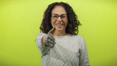 Gözlüklü bir kadın gülümseyip, parlak sarı bir arkaplan karşısında el sıkışırken arkadaşlığı ve renkli cazibeyle bağlantıyı vurguluyor..