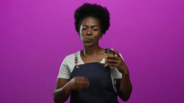 Önlüklü garson, pembe arka planda kahve fincanı tutan kamerayı öpüyor, sıcaklığını ve konukseverliğini canlı bir ortamda gösteriyor..