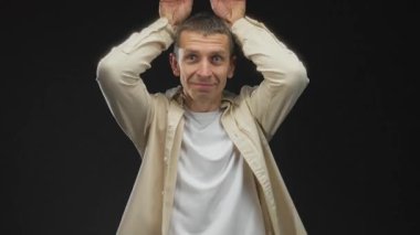 Beyaz gömlekli, siyah izole edilmiş bir arka plana karşı hareketli, neşeli ifadeli ve tavşan kulaklı beyaz bir adam..